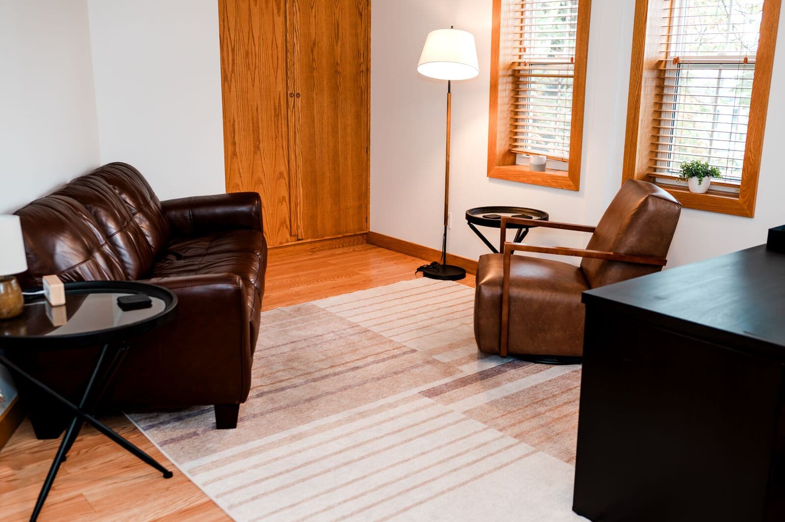 Therapy room with a leather sofa, armchair, floor lamp, and bright windows