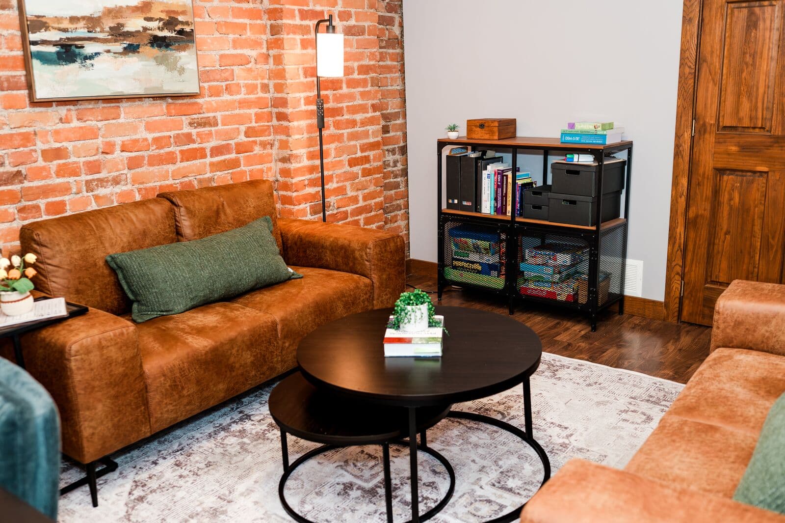 Therapy room with a leather sofa against an exposed brick wall and a shelf of books and games
